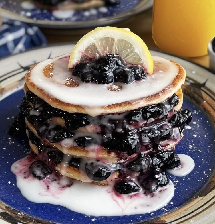 tall stack of lemon ricotta pancakes with blueberry compote syrup and lemon glaze with mimosa